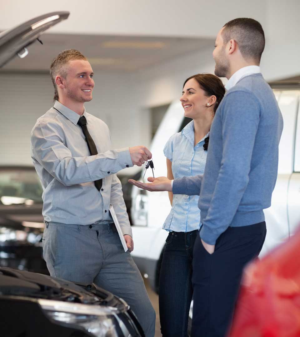 Ein Verkäufer übergibt Autoschlüssel an ein Paar beim Auto verkaufen im Autohaus